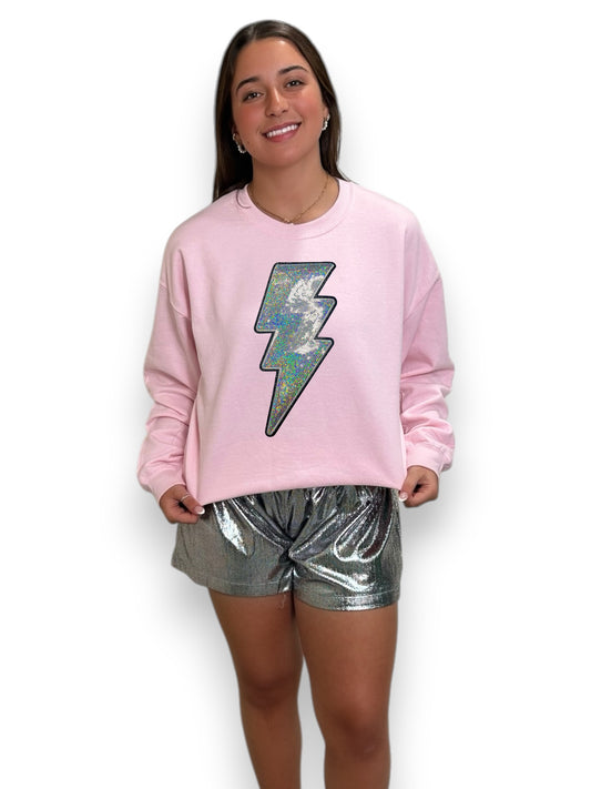 Person wearing a pink sweatshirt with a colorful lightning bolt design and silver shorts on a white background