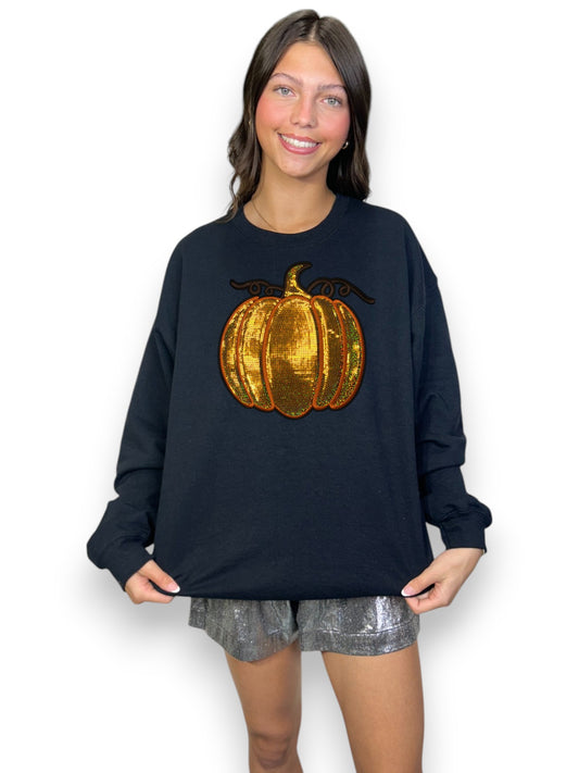 Woman wearing a black sweatshirt with a gold sequin pumpkin design on a white background