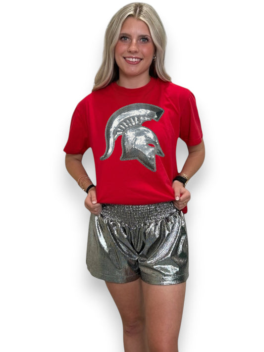 Woman wearing a red t-shirt with a silver logo and silver shorts on a white background