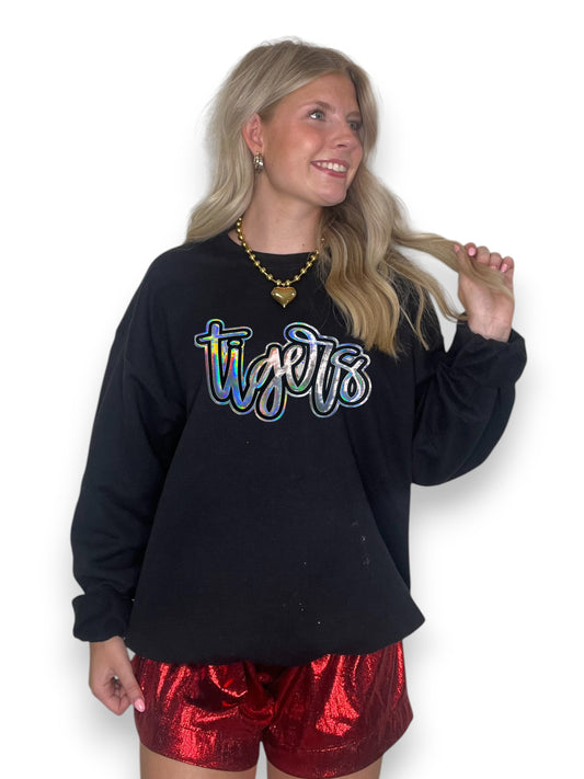 Woman wearing a black sweatshirt with 'tigers' printed on it and red shorts against a white background