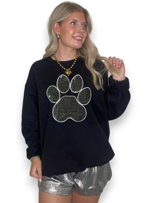 Woman wearing a black sweatshirt with a paw print design and silver shorts on a white background