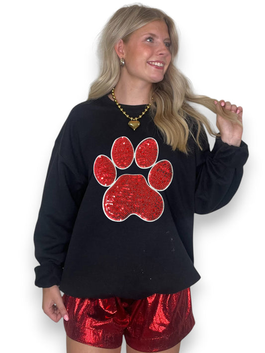 Woman wearing a black sweatshirt with a red sequin paw print design and red shorts on a white background