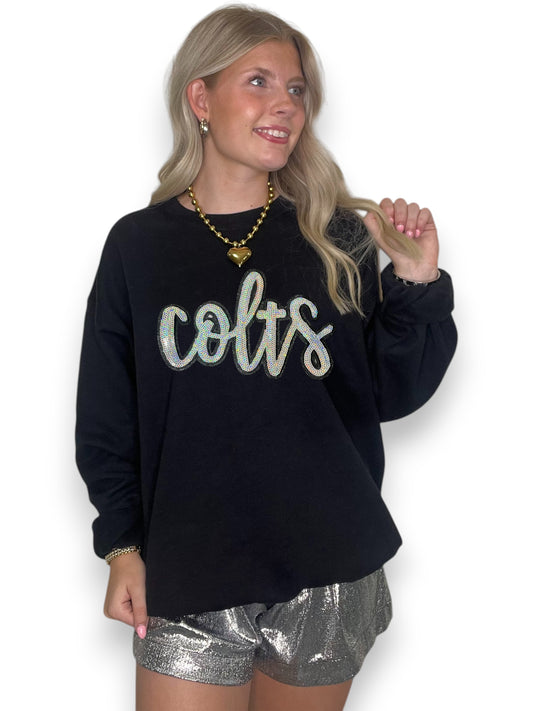 Woman wearing a black sweatshirt with 'colts' text and silver shorts on a white background