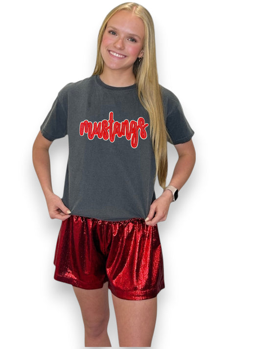 Person wearing a gray t-shirt with 'mustangs' text and red shorts on a white background
