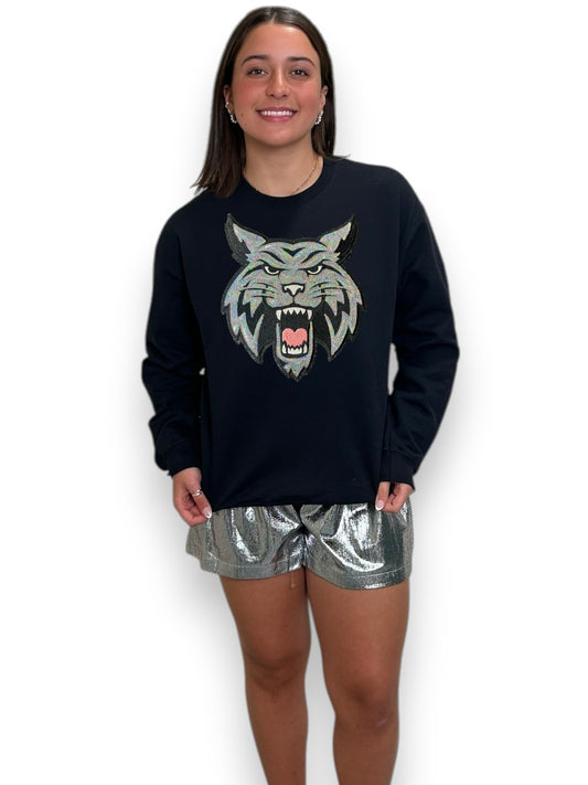 Woman wearing a black sweatshirt with a wolf graphic and metallic shorts on a white background