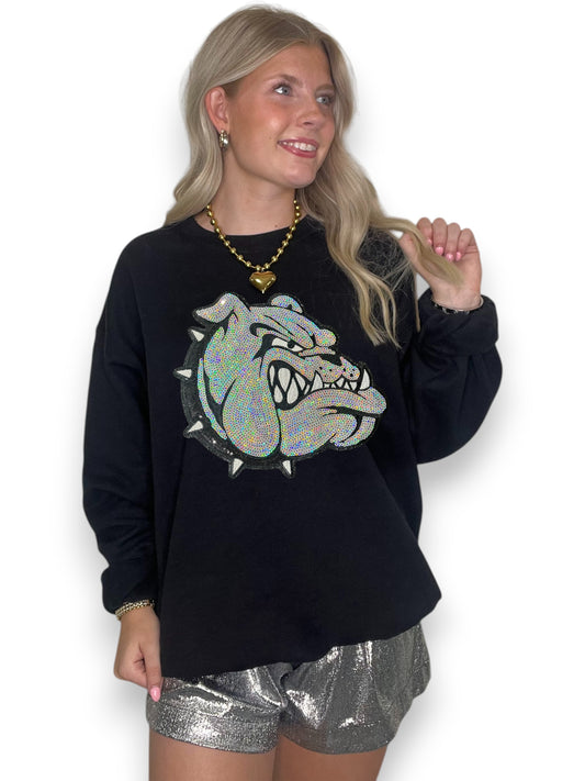 Woman wearing a black sweatshirt with a glittery bulldog graphic and silver shorts on a white background