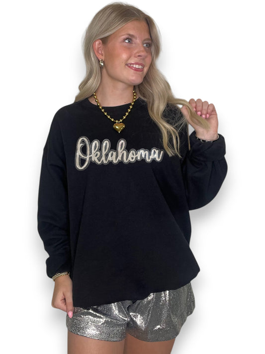 Woman wearing a black sweatshirt with 'Oklahoma' text and silver shorts on a white background