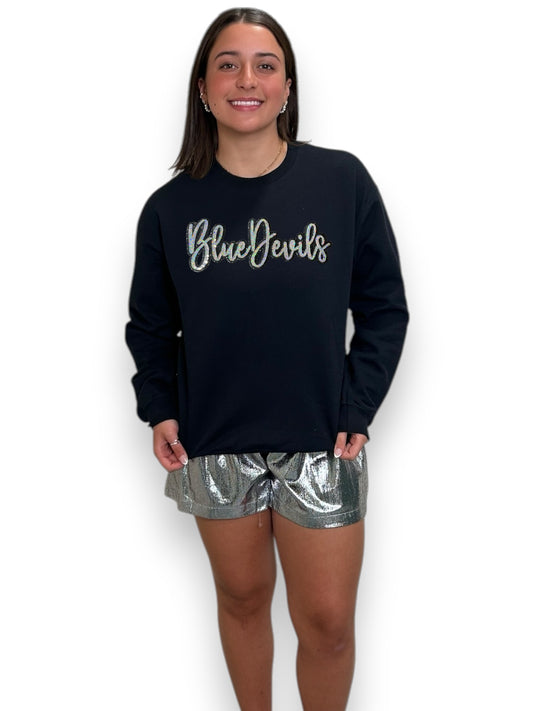Person wearing a black sweatshirt with 'Blue Devils' text and silver shorts on a white background