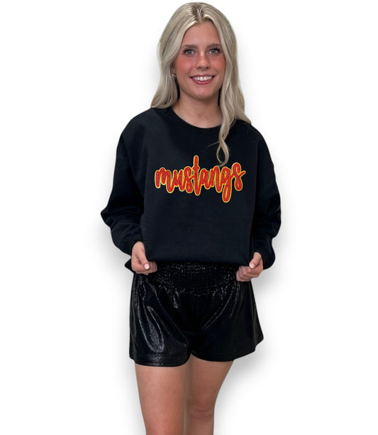 Woman wearing a black sweatshirt with 'mustangs' in orange text on a white background