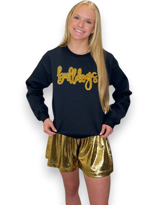 Person wearing a black sweatshirt with 'bulldogs' in gold and gold shorts on a white background
