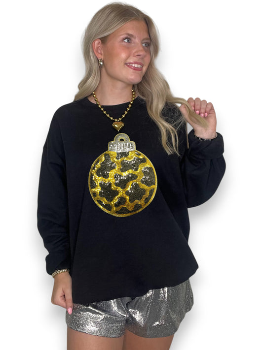 Woman wearing a black sweatshirt with a gold and silver ornament design and silver shorts on a white background
