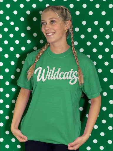 Person wearing a green 'Wildcats' t-shirt against a green and white polka dot background