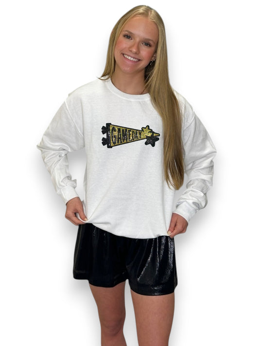 women wearing white crewneck with gold sequin patch gameday She has blonde hair and black shorts and is Infront of a white background.