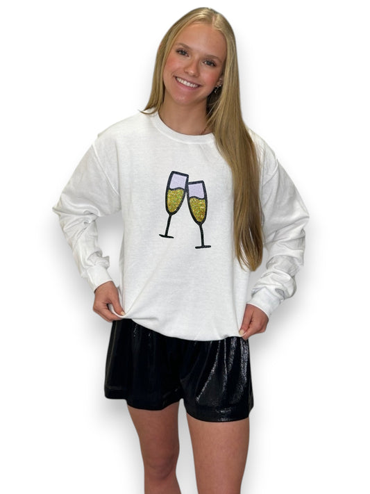 Women wearing white crewneck with champagne glasses and gold sequin black shorts with blonde hair and a white background.