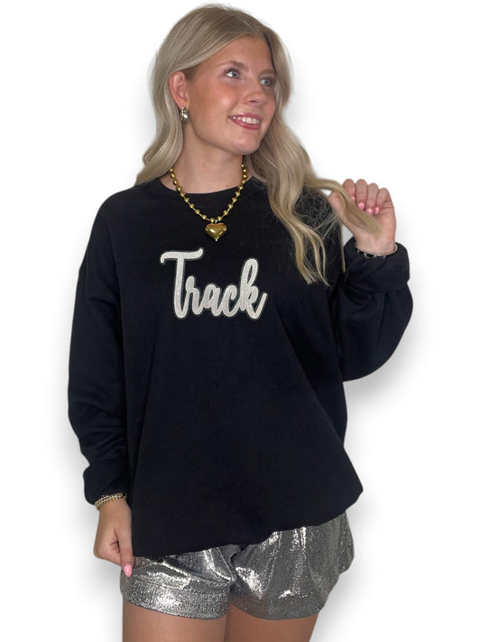 Women wearing black crewneck with white cursive sequin track patch in white shorts and in front of a white background.