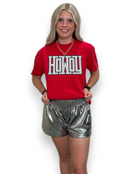 Woman wearing a red t-shirt with 'HOWDY' text and silver shorts on a white background