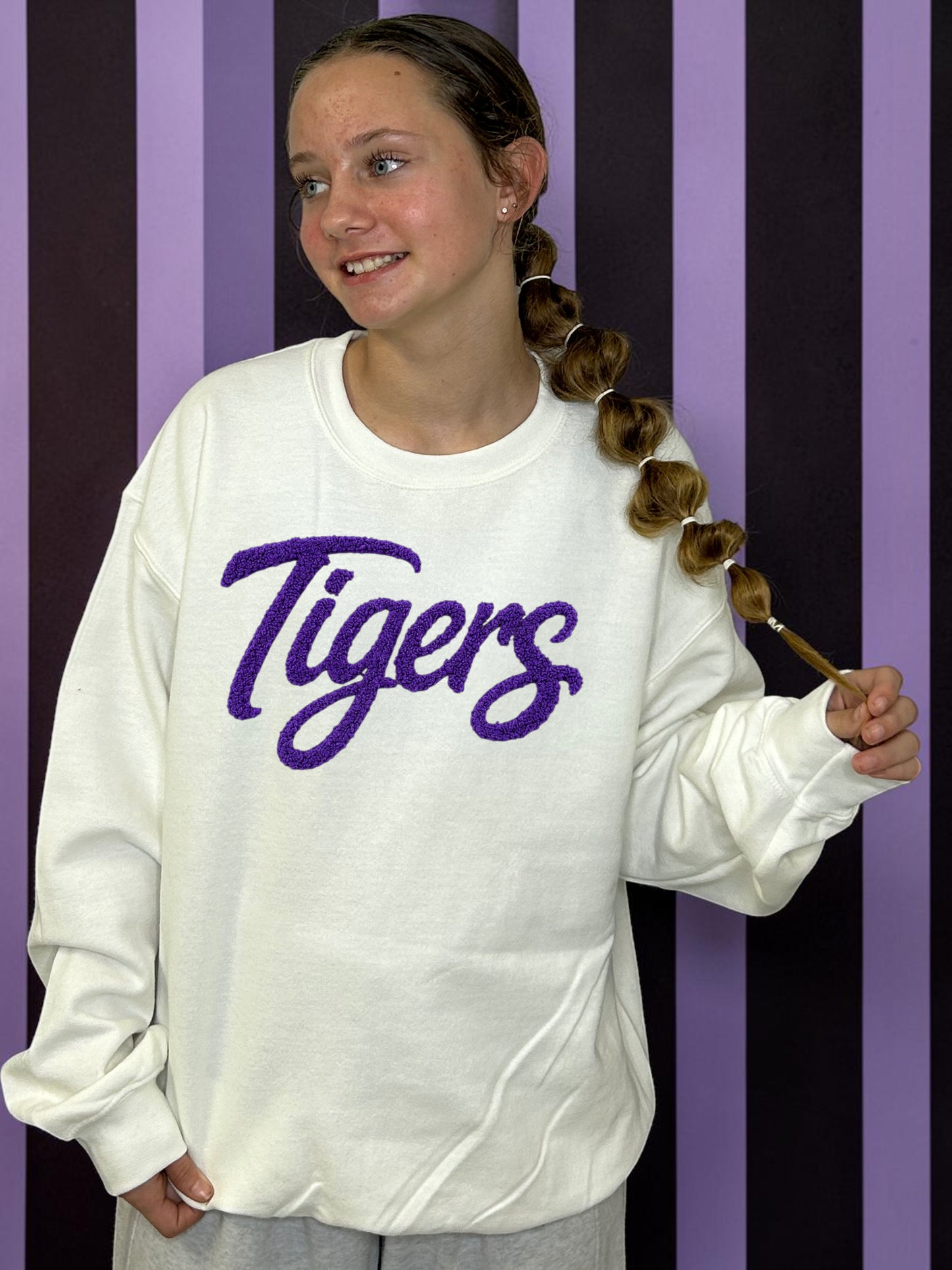 Person wearing a white sweatshirt with 'Tigers' printed in purple on a striped background
