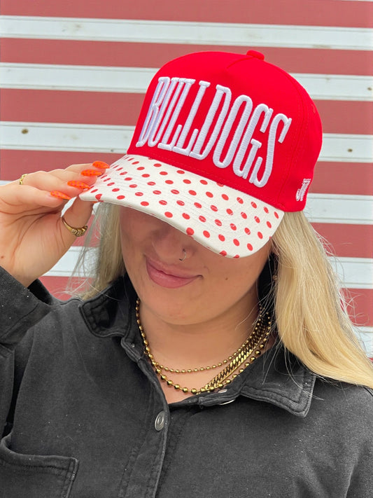Person wearing a red 'Bulldogs' cap with a polka dot visor against a striped background