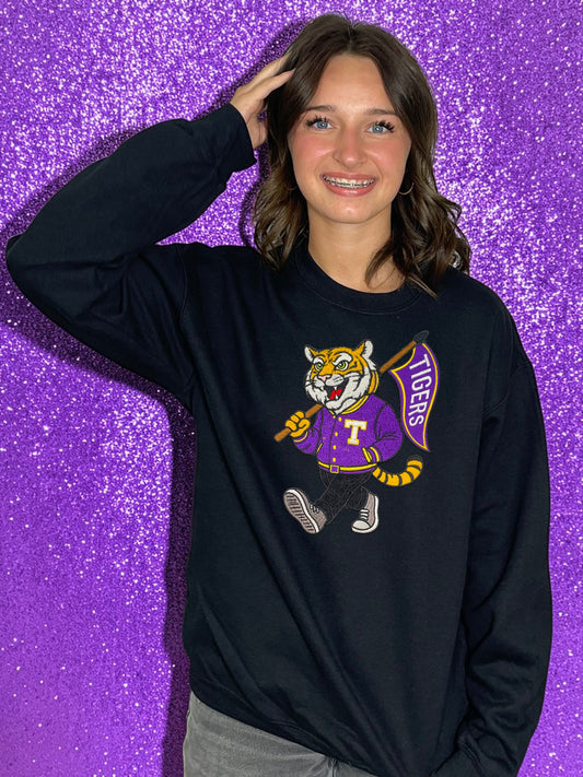 Person wearing a black long-sleeve shirt with a tiger logo on a purple glittery background